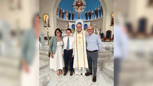 A family of four poses with a priest inside a church adorned with icons and a blue dome. The mood is joyful and celebratory.