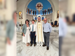A family of four poses with a priest inside a church adorned with icons and a blue dome. The mood is joyful and celebratory.