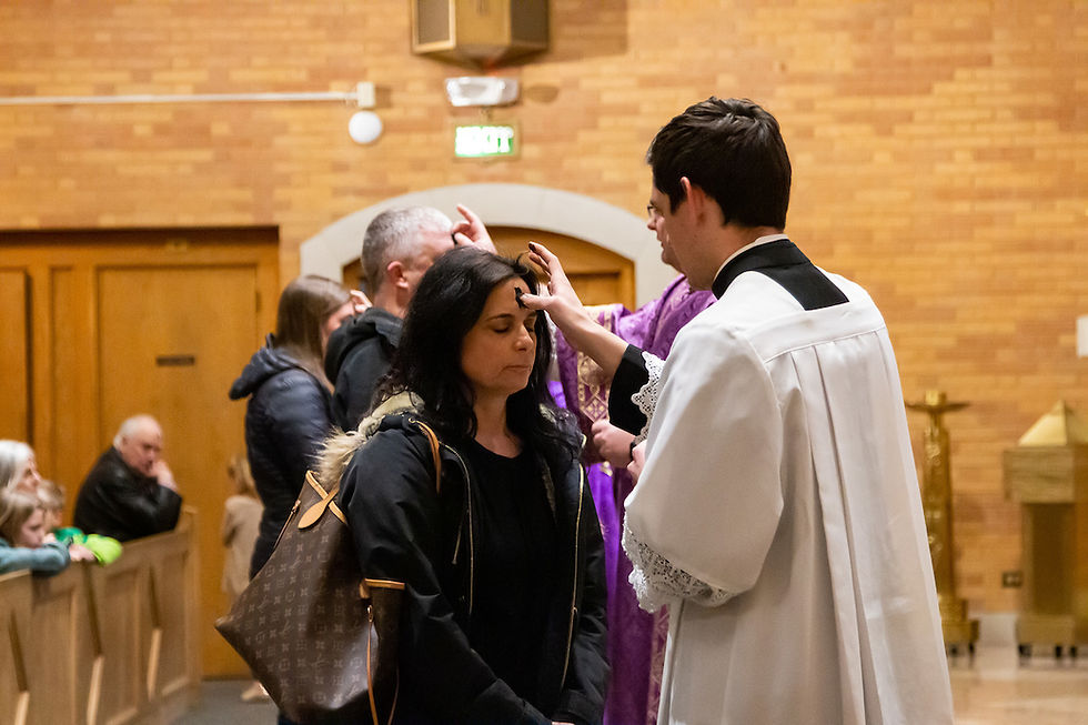 A priest applies ashes on a woman's forehead in a church. Others wait in line. The setting has brick walls and a solemn mood.