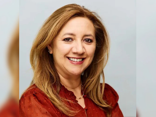 Smiling blonde woman in a red blouse posed against a light gray background, in a warm studio portrait.