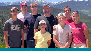 A group of eight smiling people outdoors with snowy mountains in the background. Text on shirts and "Appeal in Action" on the image.
