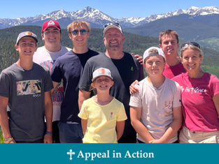 A group of eight smiling people outdoors with snowy mountains in the background. Text on shirts and "Appeal in Action" on the image.