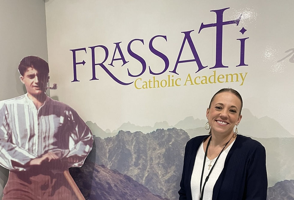 Woman smiling next to a cardboard cutout of a man. Background shows "FRASSATI Catholic Academy" text, with mountain imagery. Calm mood.