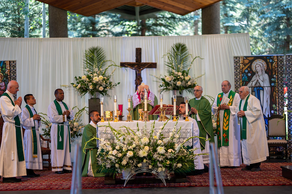 Clergy in green vestments conduct a Catholic Mass at an altar with candles and flowers, under a crucifix, in a church with stained glass.