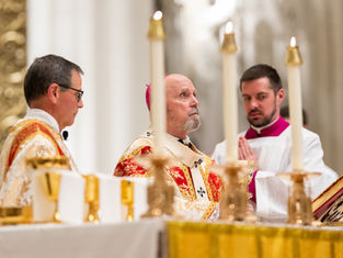 Three clergy in ornate robes during a religious ceremony. Candles are lit in a grand setting, with solemn expressions and focus.