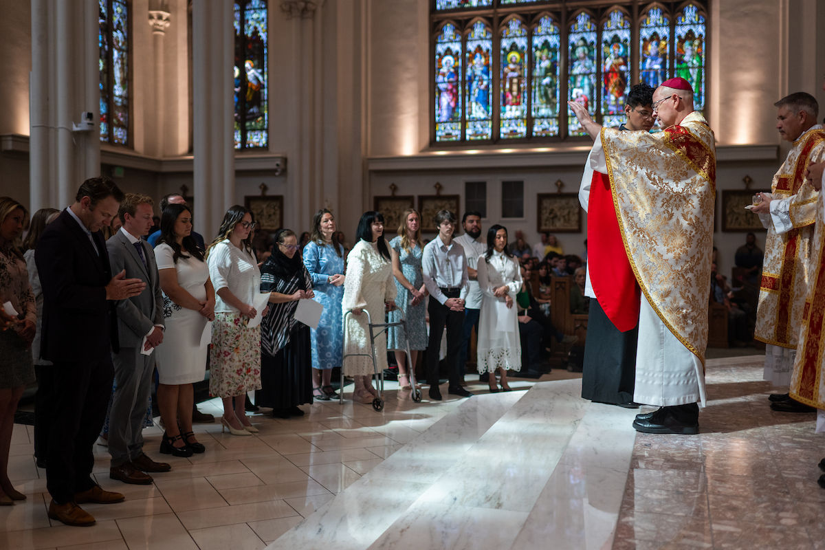 A bishop blesses a line of people standing at the front of the church during Mass.