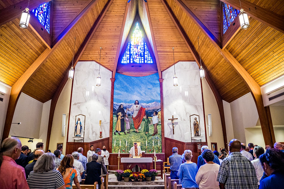 Congregation stands during Mass in a wood-paneled church, facing a priest at the altar beneath a large mural and stained glass.