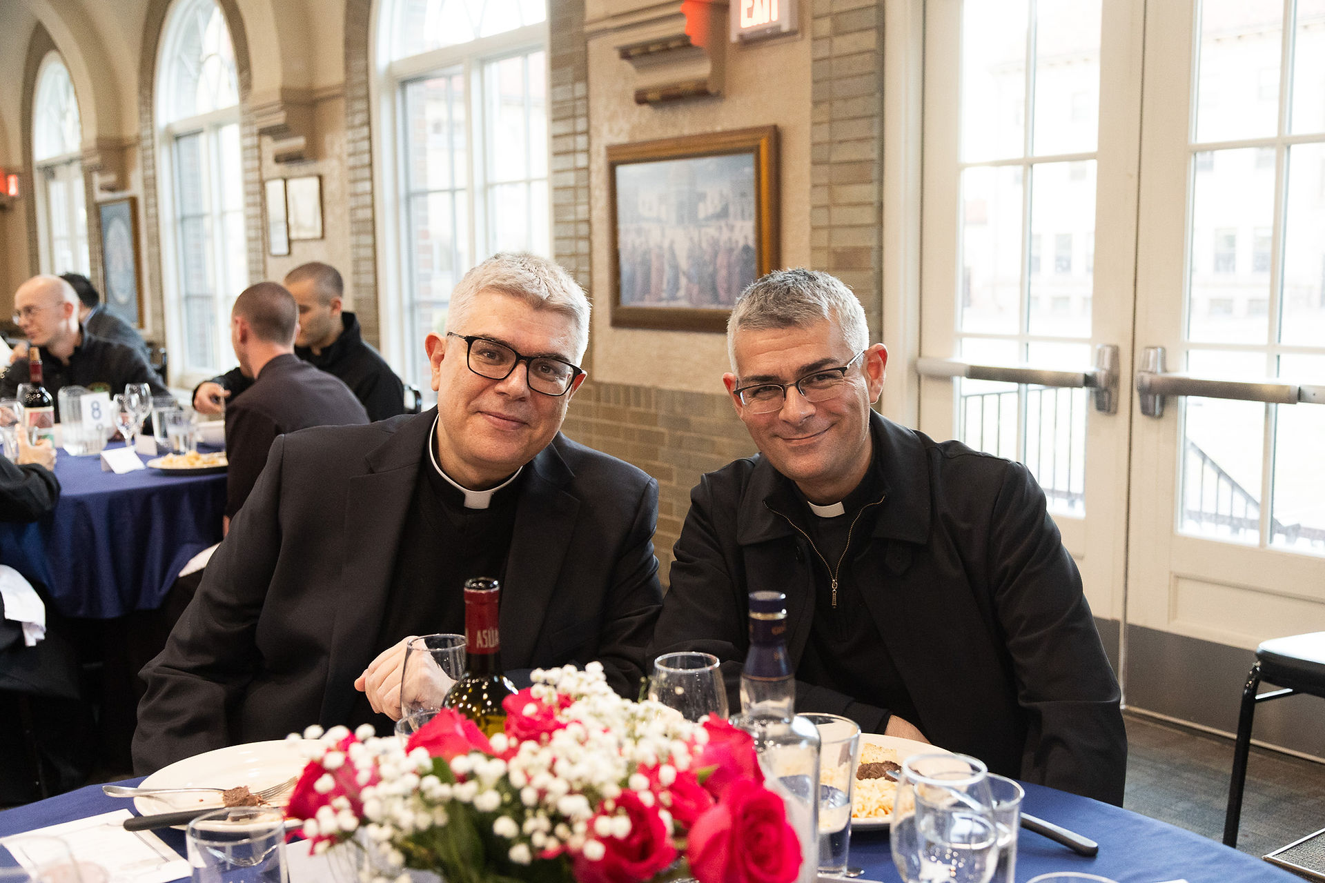 Two priests smile for a picture at a reception following Mass.