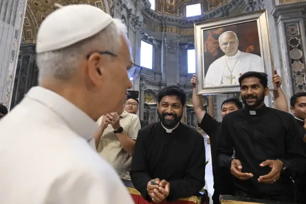 A religious figure smiles at a group of men inside a grand building. One man holds a large portrait. The mood is joyful and reverent.