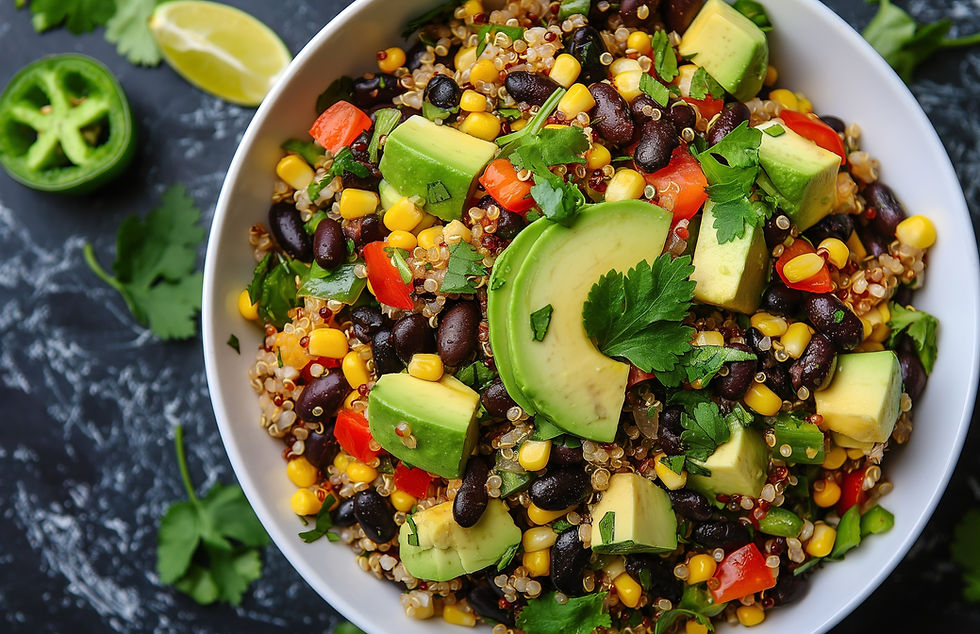 Quinoa salad in a bowl with avocado, black beans, corn, red peppers, cilantro; lime and jalapeño slices nearby on black marble.
