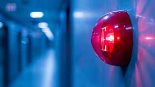 Red alarm light on a blue wall in a corridor, glowing brightly. The background is blurred, creating a tense, urgent mood.