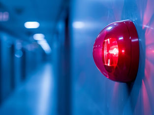 Red alarm light on a blue wall in a corridor, glowing brightly. The background is blurred, creating a tense, urgent mood.