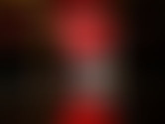 Person in red ornate robe sits in a wooden chair, hands clasped. Floor reflection visible. Calm mood, no text.