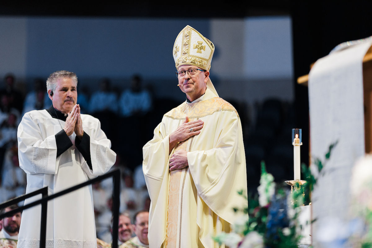 A bishop stands in prayer with hand over his heart during the Mass.