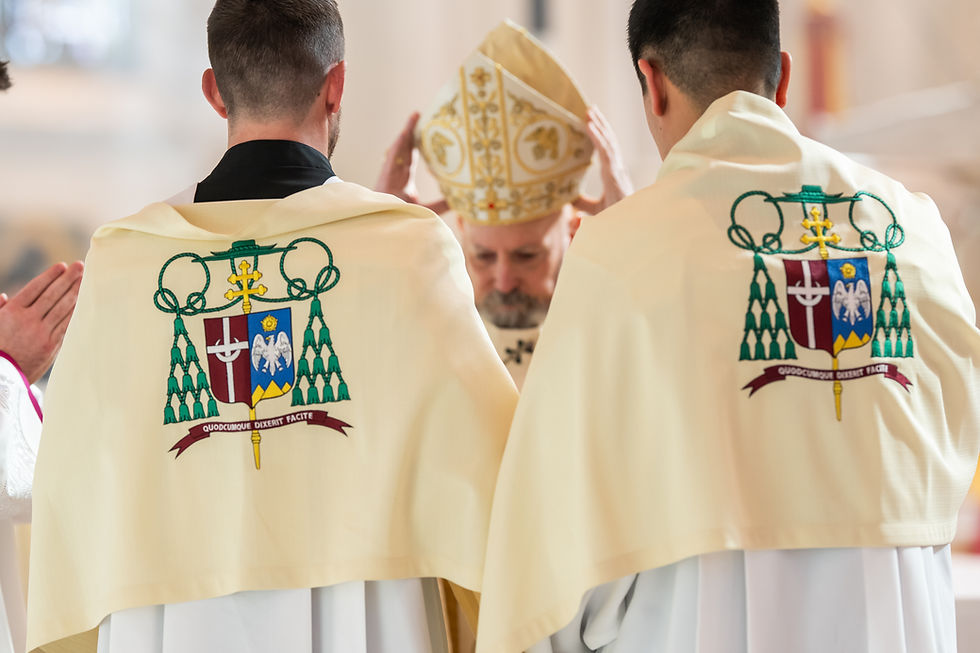 Two clergy in decorated ivory vestments stand with a bishop holding a mitre. Symbols and Latin text are visible. Reverent setting.