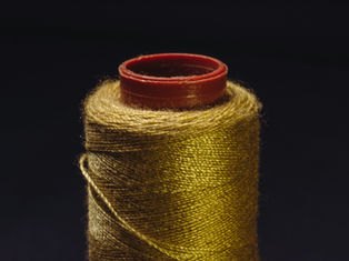 Close-up of a spool of golden thread with a deep red top against a dark background, highlighting the thread's sheen and texture.