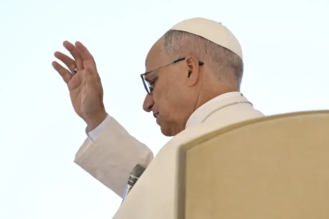 A person in white attire raises their hand in a blessing gesture. The background is plain, creating a serene and solemn atmosphere.