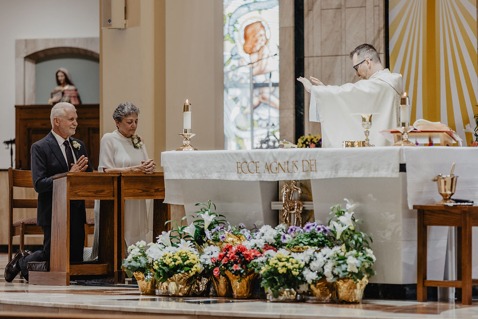 A couple kneels at a church altar with flowers, a priest raises hands in prayer. "ECCE AGNUS DEI" text on the altar cloth. Peaceful mood.