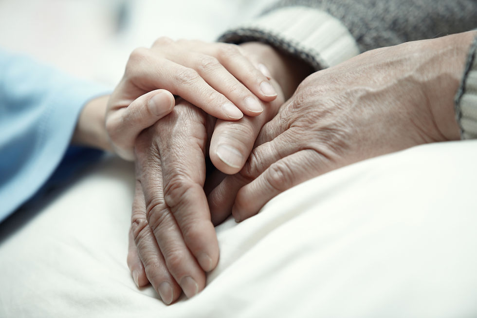 Hands of an elderly person being gently held by a younger person on a white blanket, conveying warmth and care in a soft-focus setting.