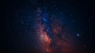 Starry night sky showing the Milky Way with vibrant blues and oranges. Dark, vast setting evokes wonder and serenity. No text visible.