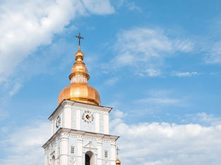 White clock tower with golden domes against a clear blue sky. The tower has Roman numerals. Bright and peaceful atmosphere.