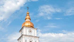 White clock tower with golden domes against a clear blue sky. The tower has Roman numerals. Bright and peaceful atmosphere.