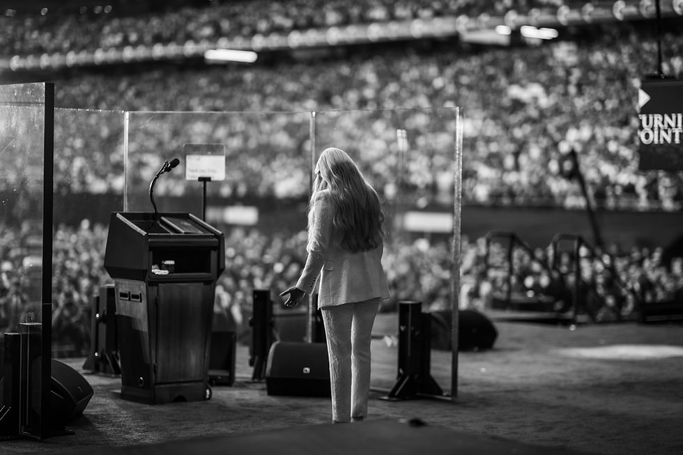 Audience and speaker on a stage with a podium under bright lights. Packed stadium in background. Black and white, text: "TURN POINT."