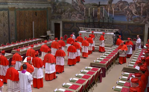 Cardinals in red robes gather in an ornate hall with frescoed walls and candles. They are seated at arranged tables, creating a solemn atmosphere.