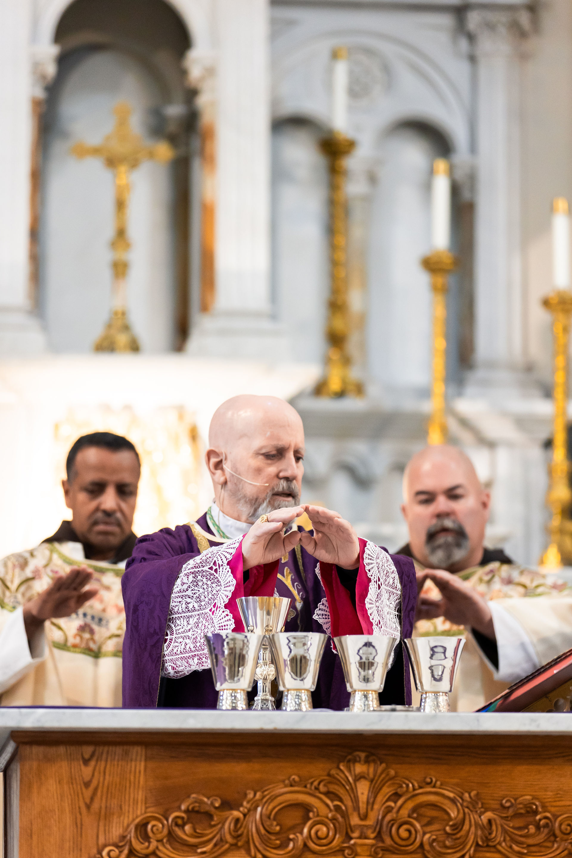 Clergy in ornate robes perform a religious ceremony with silver cups on an altar. The ornate church interior adds a solemn atmosphere.