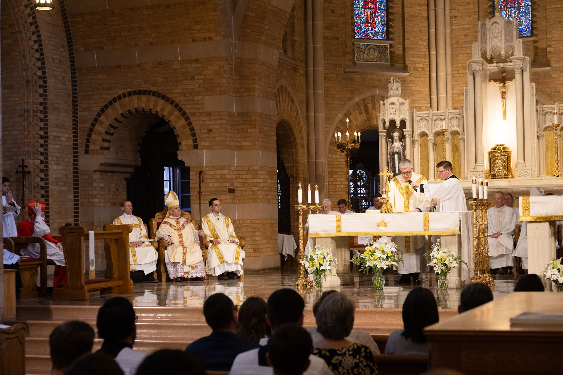 A priest stands at an altar during a religious ceremony in a beautiful, ornate chapel. The mood is celebratory and excited.