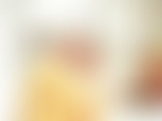 Pope St. John Paul II, vested in yellow and white robes, holds a cross, eyes closed in prayer. Background features blurred floral decorations. Peaceful atmosphere.