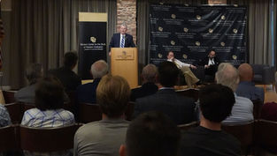 A speaker at a podium addresses an audience in a conference room. "Benson Center for the Study of Western Civilization" banner is visible.