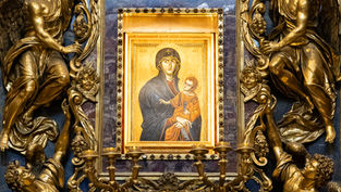 Ornate gold religious altar with angels around a blue-framed Madonna and Child icon, Greek letters visible, solemn and reverent