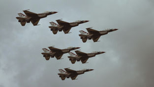 Six jet planes in formation fly against a cloudy sky, showcasing sleek designs with red and white patterns, evoking a sense of precision.