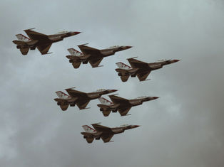 Six jet planes in formation fly against a cloudy sky, showcasing sleek designs with red and white patterns, evoking a sense of precision.