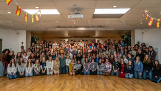 Group of people smiling in a room with wooden floors. Spanish flags hang from ceiling. Two signs read "Abortion Betrays Women" and "The Future is Anti-Abortion".