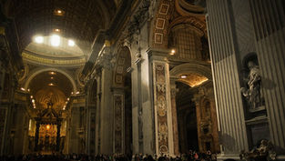 Inside a grand cathedral with ornate columns and arches, people walk beneath intricate ceilings. Warm lighting and statues create a solemn mood.
