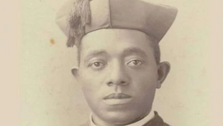 A man in a clerical outfit and cap looks directly at the camera. The image has a sepia tone, with a plain background, conveying a formal mood.