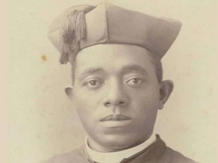 A man in a clerical outfit and cap looks directly at the camera. The image has a sepia tone, with a plain background, conveying a formal mood.