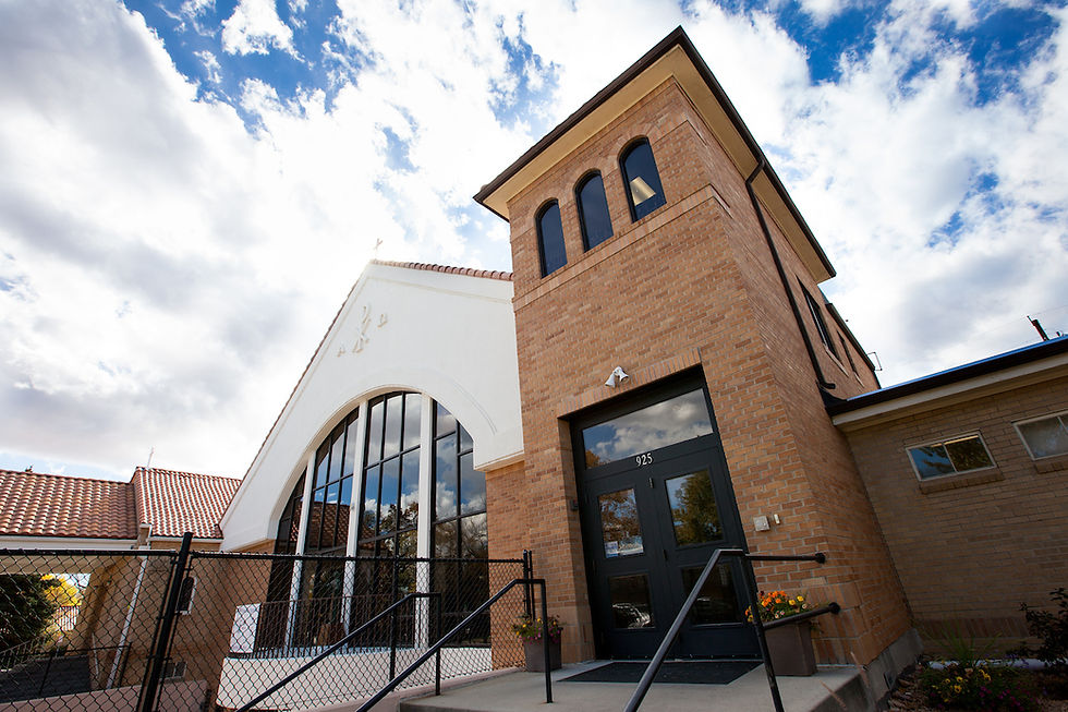 Brick and white church with arched windows against a blue sky, entrance labeled "925," surrounded by a black fence and potted flowers.