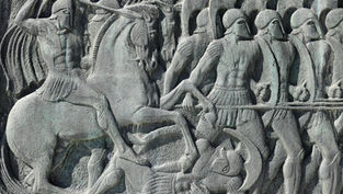 Ancient stone relief of warriors in helmets; one on horseback attacking with spear, others marching. Gray tones, evokes historical battle.