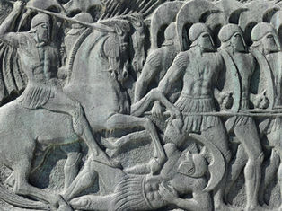Ancient stone relief of warriors in helmets; one on horseback attacking with spear, others marching. Gray tones, evokes historical battle.