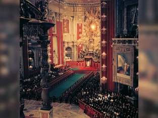 Ornate church interior with a large gathering of people. Red and gold decor dominates. Illuminated altar and religious art visible.