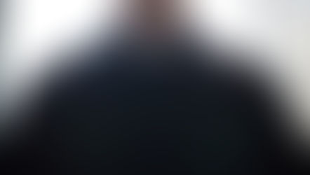 Close-up of a person wearing a black clerical shirt with a white collar. Bright light illuminates the background, creating a serene mood.