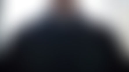 Close-up of a person wearing a black clerical shirt with a white collar. Bright light illuminates the background, creating a serene mood.