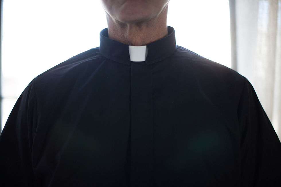 Close-up of a person wearing a black clerical shirt with a white collar. Bright light illuminates the background, creating a serene mood.
