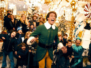Elf-costumed man joyfully leads excited crowd in festive, decorated store with Christmas trees, lights, and gifts; cheerful atmosphere.