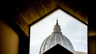 View of a domed cathedral roof framed by a geometric window. The sky is partly cloudy, creating a serene atmosphere. No text visible.
