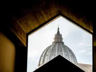 View of a domed cathedral roof framed by a geometric window. The sky is partly cloudy, creating a serene atmosphere. No text visible.