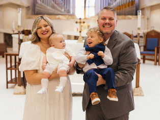 Smiling parents hold two dressed-up children in a church before the altar, creating a joyful family portrait.
